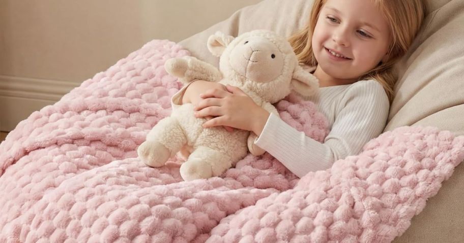 Little girl cuddling with a stuffed lamb with a plush pink blanket