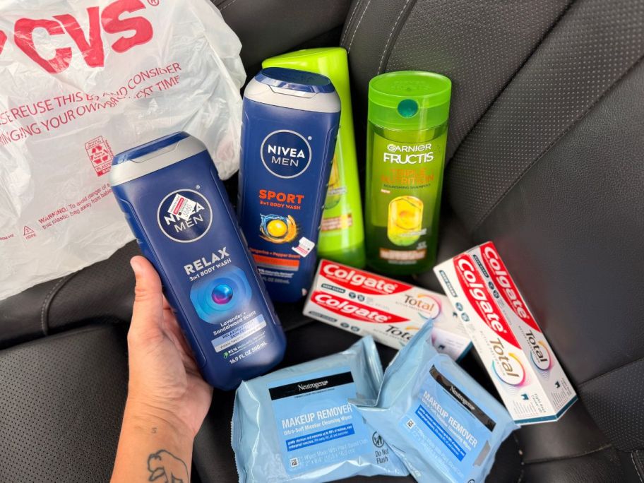 A pile of products next to a CVS bag including Nivea Body Wash, Garnier Hair Care, Colgate toothpaste and Neutrogena Towelettes