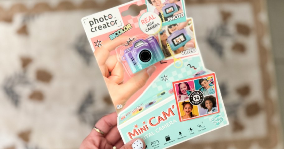 A hand holding a colorful toy camera in the package.