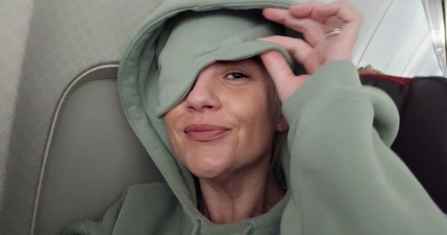 woman wearing green comfrt brand travel hoodie with sleep mask inside hood on airplane