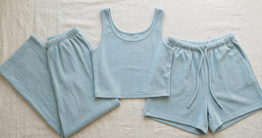 A light blue ribbed tank top with matching ribbed shorts and pants laid out on a light background.