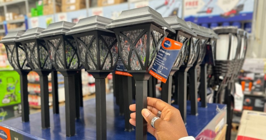 A hand holding a black Harbor Breeze LED path light in a store display.