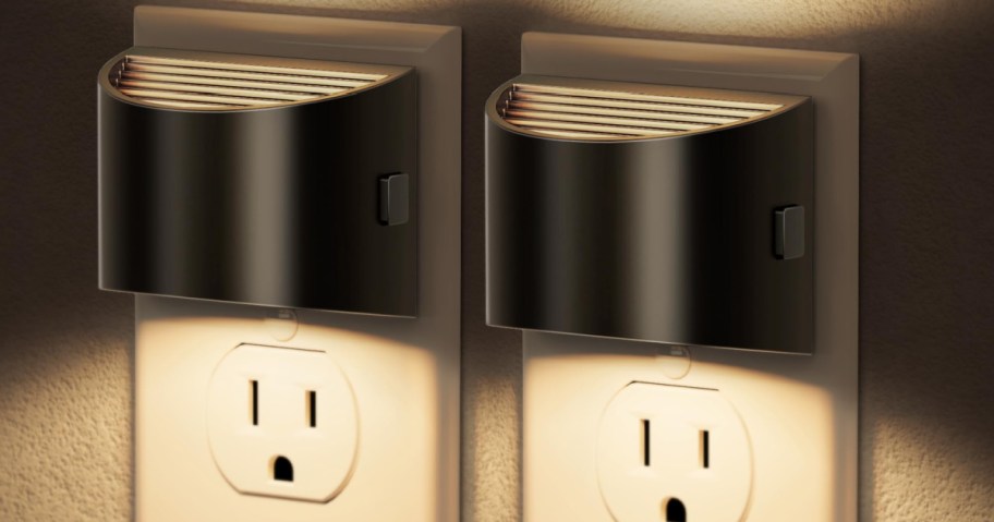 Two black plug-in night lights plugged into wall outlets, emitting warm light.