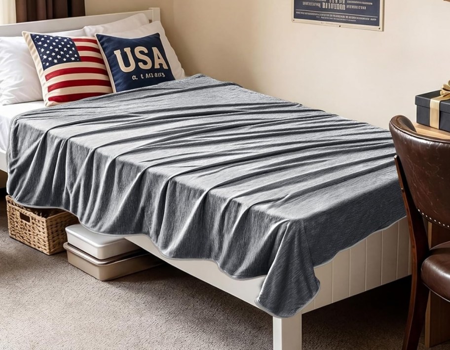 a twin bed with a gray blanket draped over it