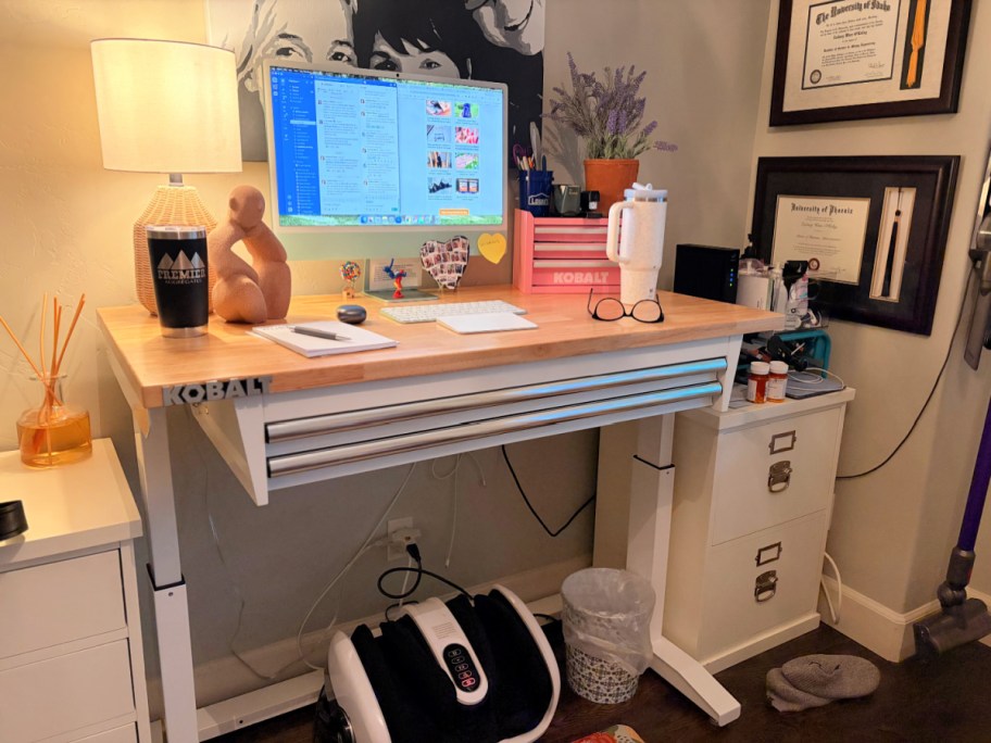 Kobalt work bench with a computer and desk accessories on top next to a file cabinet and degrees in a decorated work space