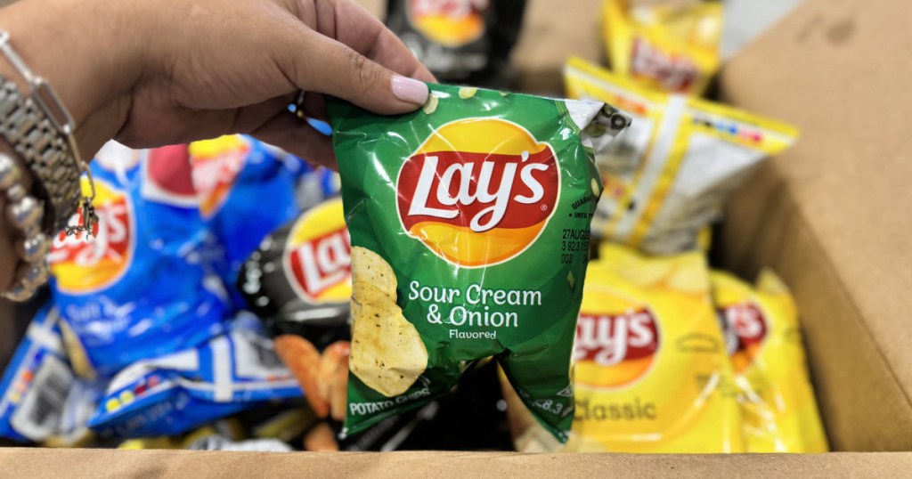 Hand holding bag of sour cream and onion, lays potato chips