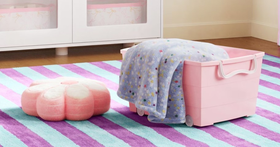 pink storage box with blanket and pillow on a striped rug