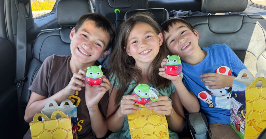3 kids in the backseat of a car holding up McDonald's Squishmallows