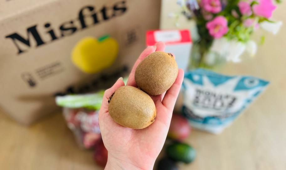 hand holding kiwis in front of misfits market box
