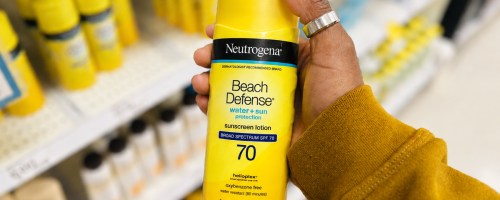 hand holding a yellow bottle of Neutrogena Beach Defense Sunscreen in store