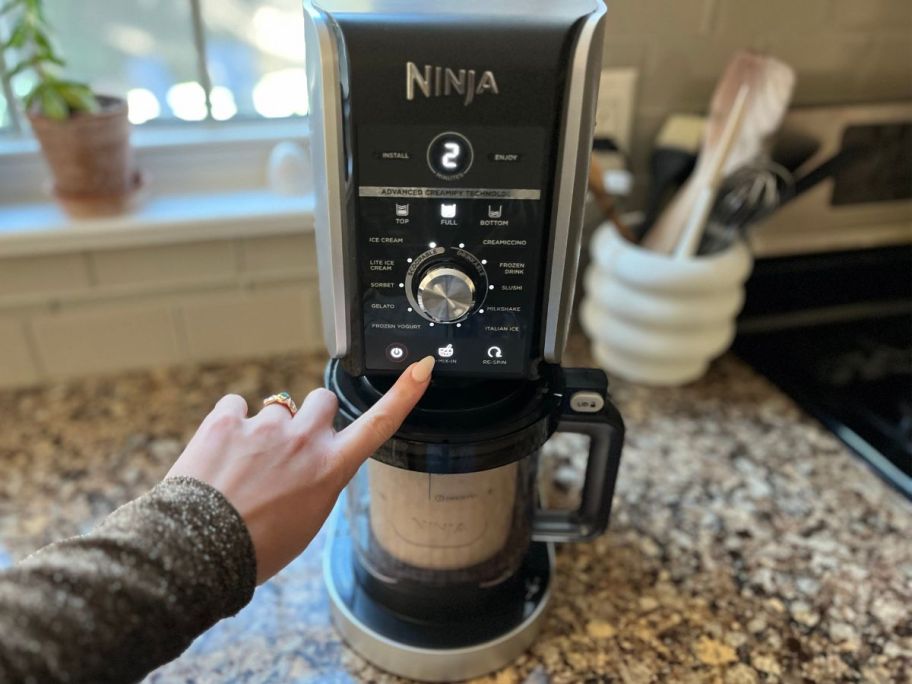 Hand pushing the button on a Ninja Creami Deluxe