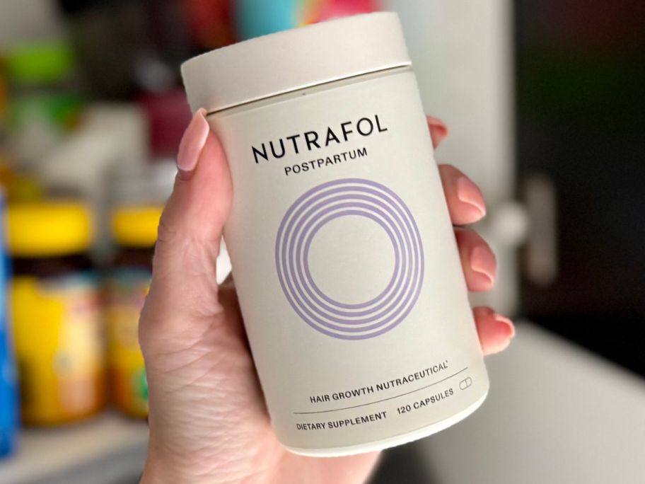 hand holding Nutrafol Women's Postpartum Hair Growth Nutraceutical Supplement bottle in kitchen