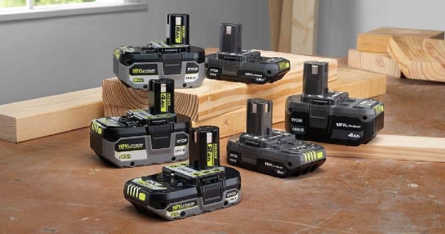Several Ryobi One+ HP 18V lithium-ion batteries of varying capacities arranged on a wooden workbench among pieces of lumber.