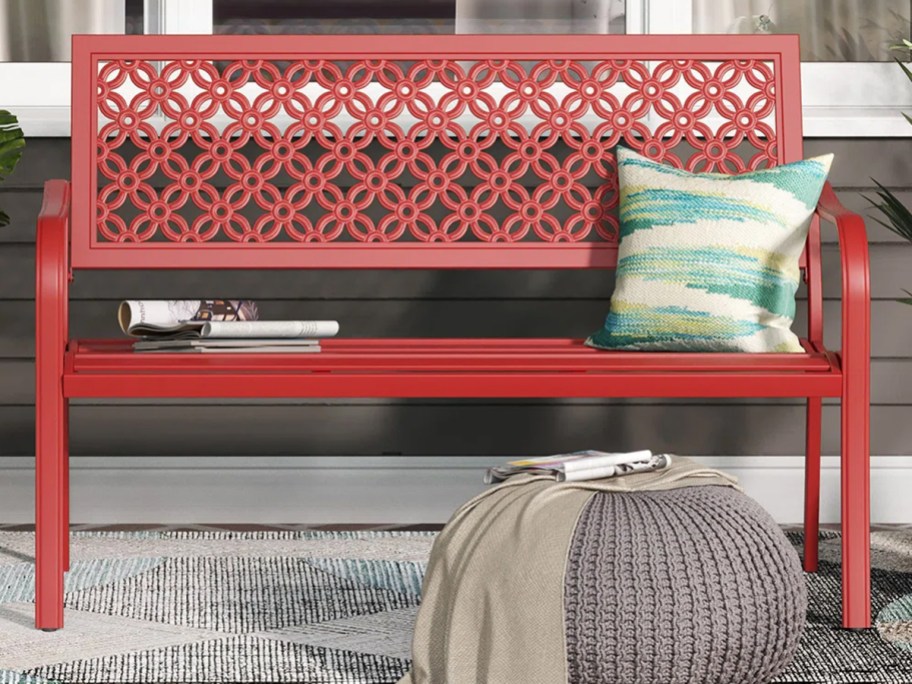 red garden bench with a green throw pillow and books on it