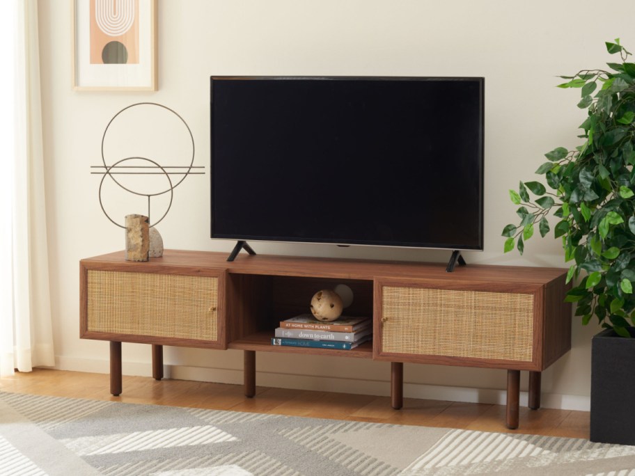 A wooden media console with two woven cane cabinets and an open central shelf holding a television, books, and decorative accents in a styled living room.