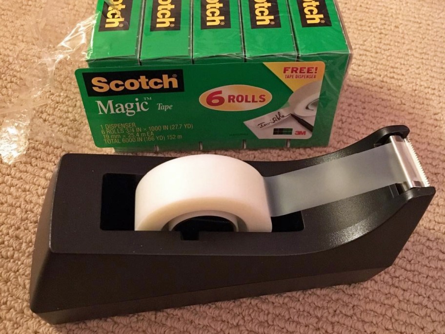 black tape dispenser with green boxes of tape refills in background