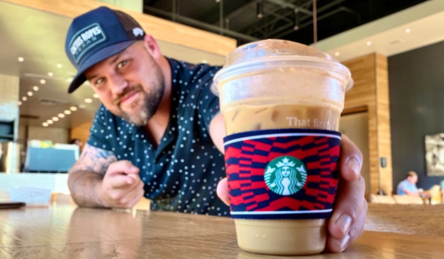 main pointing to a starbucks cup with a sleeve on it