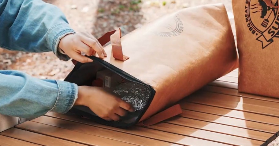 person pulling a foil wrapped brisket out of an insulated meat blanket bag