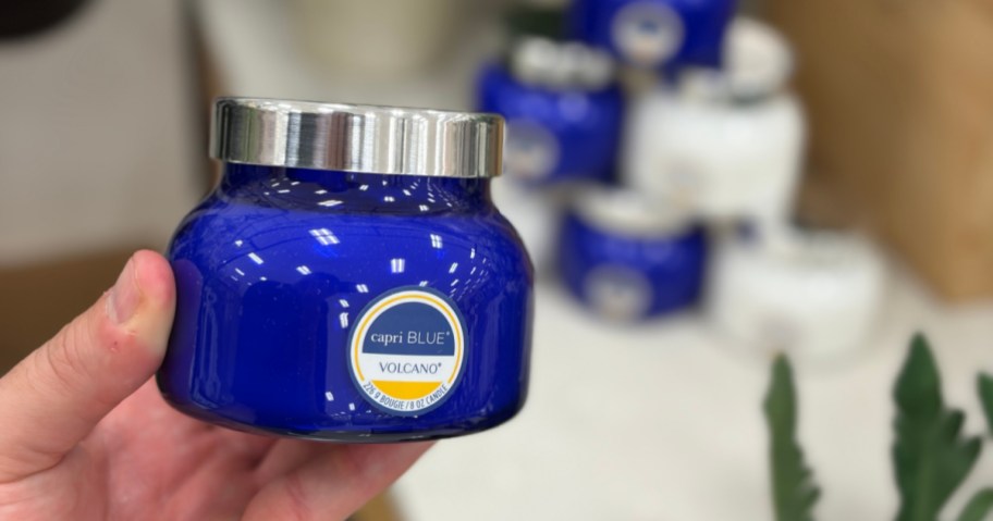 A hand holding a blue jar of Capri Blue Volcano candle.