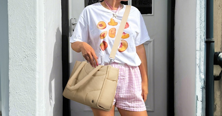 woman in a white tee and pink shorts with a tan crossbody bag