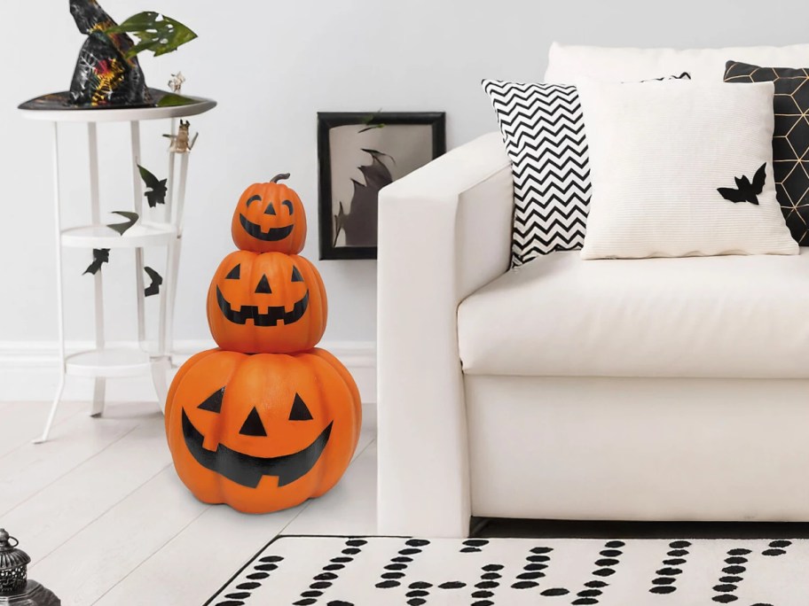 A stack of three smiling orange jack-o'-lanterns sitting on the floor next to a white sofa.