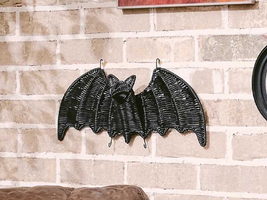 A black woven bat wall decoration hanging on a light brick wall.