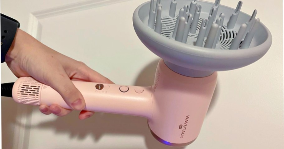 A person holding a pink hair dryer with a diffuser attachment.