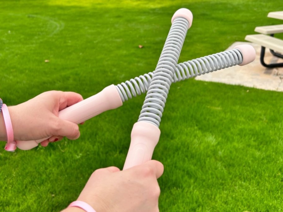 hands holding light grey and pink battle ropes