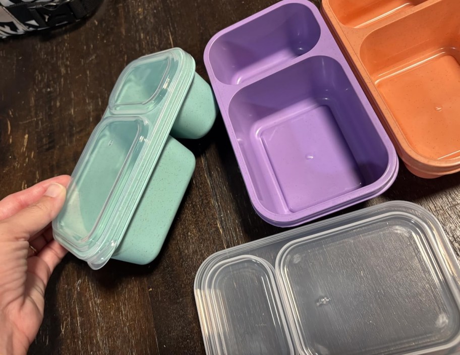 hand holding a blue snack pack container with purple and orange on table