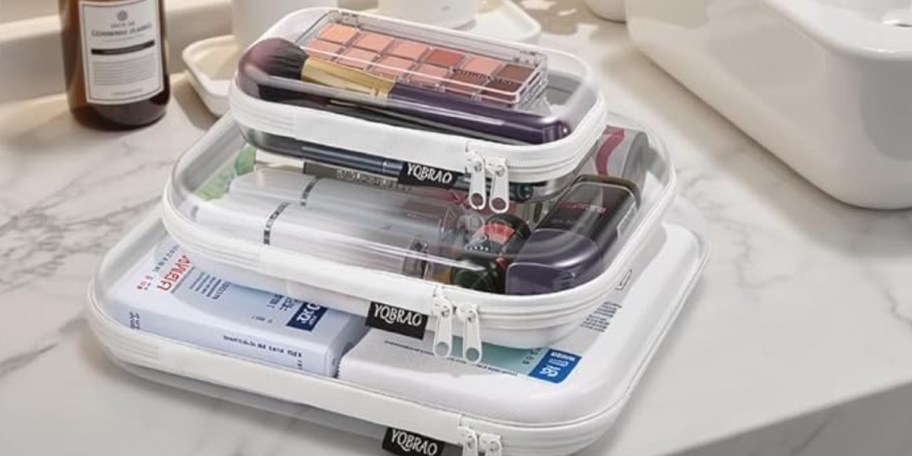 three clear zipper cases full of toiletries stacked on table