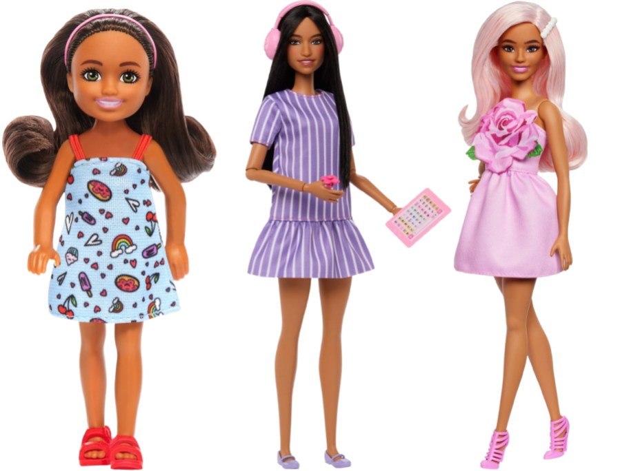 Three Barbie dolls standing side-by-side against a white background; a small doll in a light blue patterned dress on the left, a dark-haired doll in a purple striped dress holding a pink tablet in the middle, and a pink-haired doll in a pink dress with a large rose detail on the right.