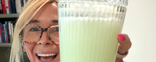 woman holding green protein drink in ribbed glass with lid and straw