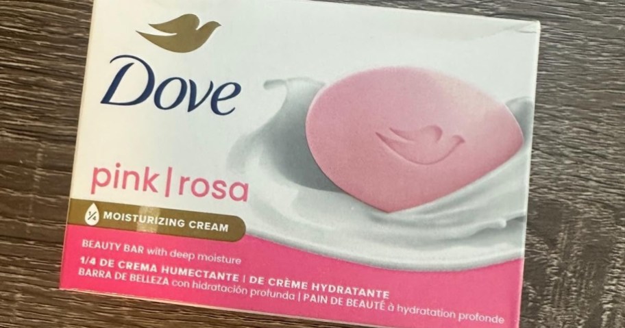 A close-up of a Dove pink beauty bar soap box resting on a wooden surface.