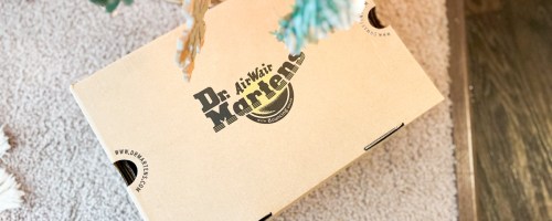 A closed Dr. Martens cardboard shoebox sitting on a beige rug beneath a decorated tree.