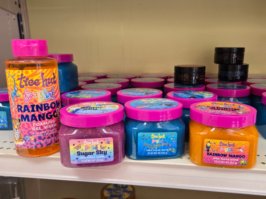 A store shelf displaying colorful Tree Hut and Lisa Frank bath products, including a bottle of Rainbow Mango foaming gel wash and jars of Sugar Sky, Ocean Pop, and Rainbow Mango shea sugar scrubs.