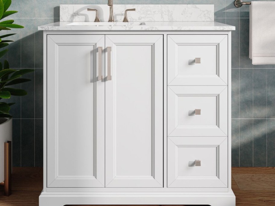 A white bathroom vanity with a marble countertop, two cabinet doors, three drawers, and silver hardware.