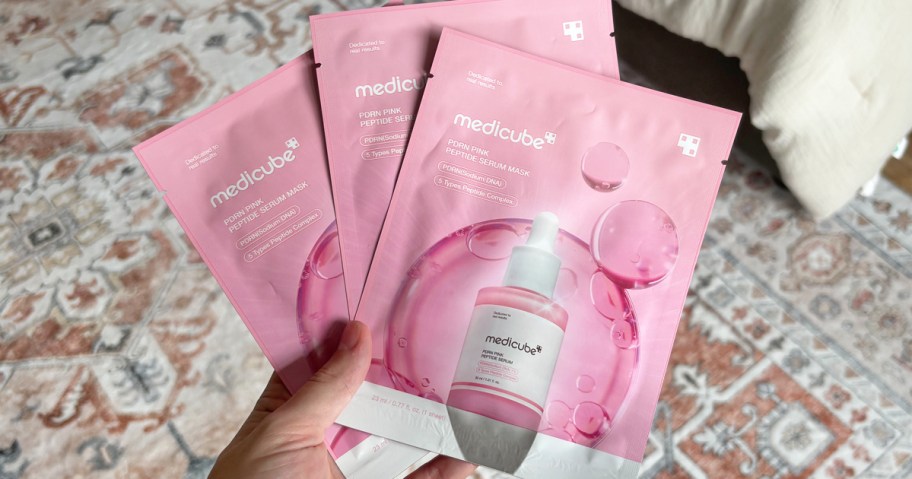 hand holding 3 medicube PDRN Pink Peptide Ampoule Mask packets