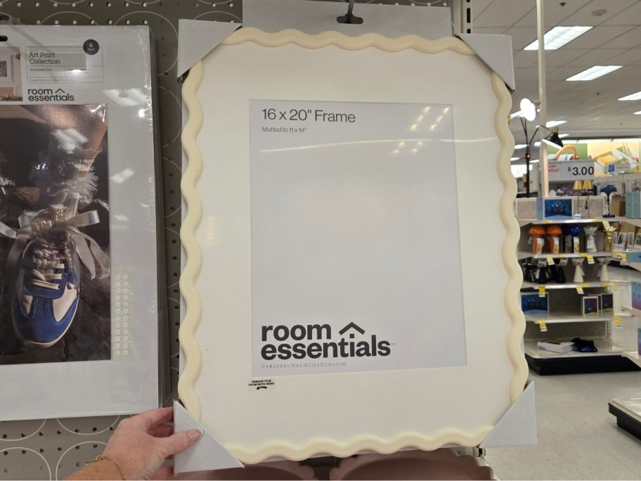 a hand holding the corner of a white scalloped picture frame with mat