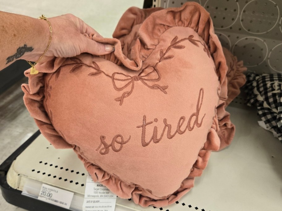 womans hand holding a heart shaped throw pillow