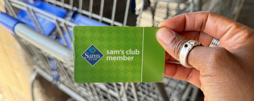 hand holding a Sam's Club Membership card in front of a shopping cart