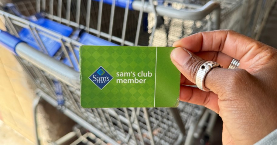 hand holding a Sam's Club Membership card in front of a shopping cart