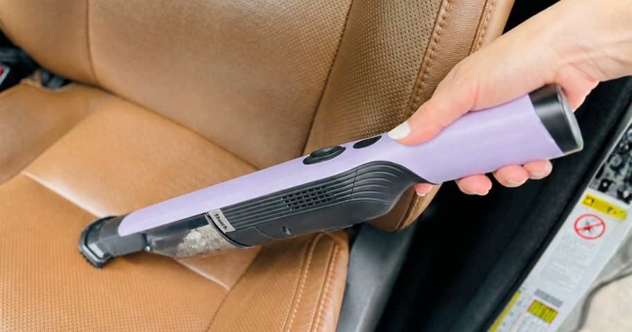 hand using a Shark WandVac cordless hand vacuum to clean a car seat