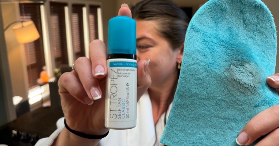 A person holding a bottle of tanning product and a blue tanning mitt.