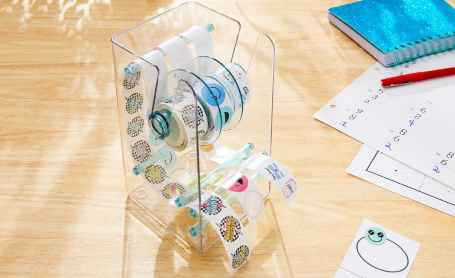 a sticker dispenser on a desk next to some school work