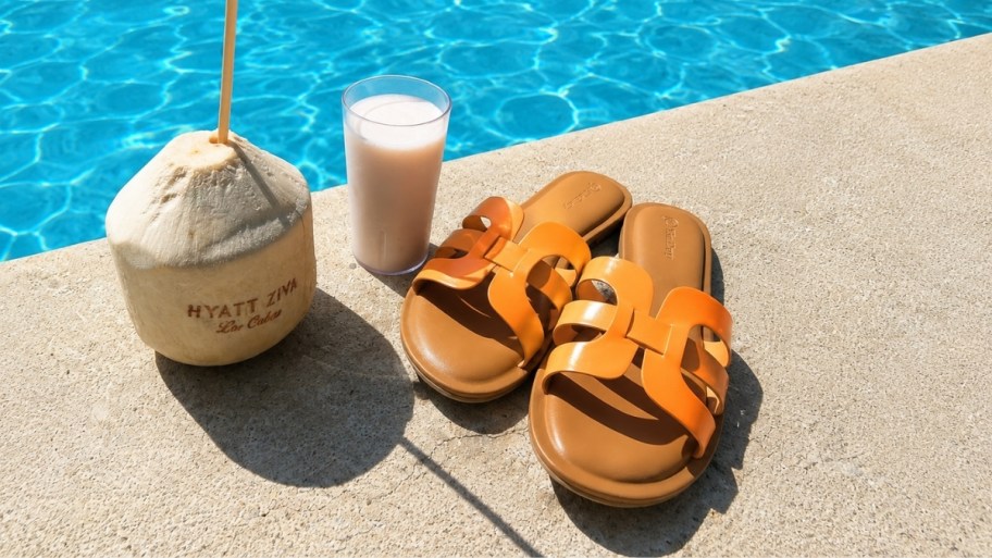 a pair of orange slide sandals next to a pool
