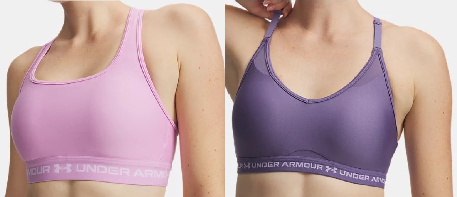 Two people side-by-side modeling Under Armour sports bras against a light background: one wearing a light pink sports bra on the left, and the other wearing a purple V-neck sports bra with thin straps on the right.