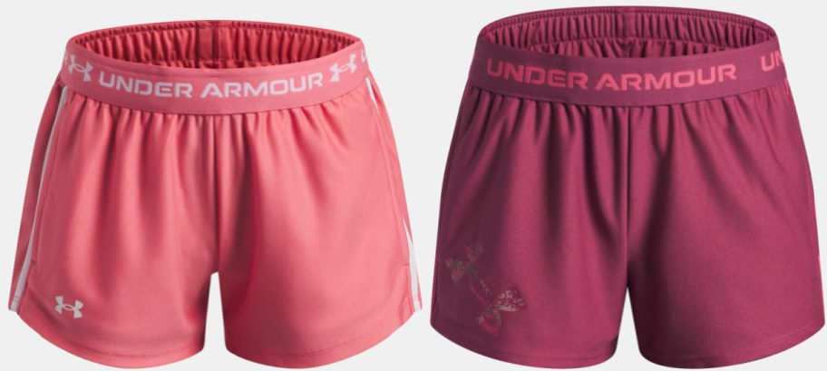 A pair of pink Under Armour athletic shorts with white side stripes and a pair of dark pink shorts with the brand name on the waistband.