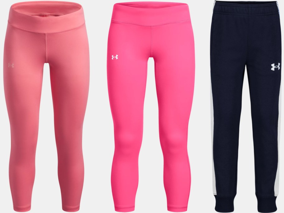 A set of Under Armour pants including light pink leggings, bright pink leggings, and dark blue sweatpants with white side stripes.