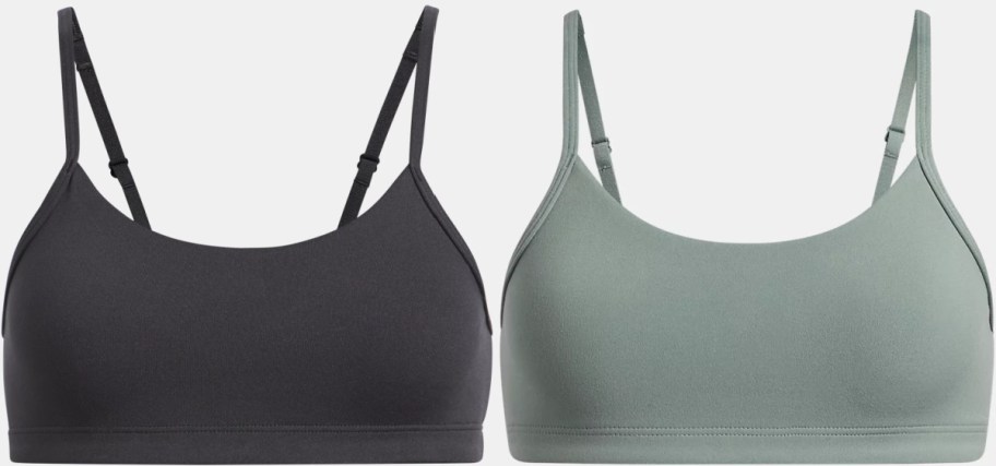 A pair of Under Armour sports bras, one black and one sage green, with thin adjustable straps and a scoop neckline.