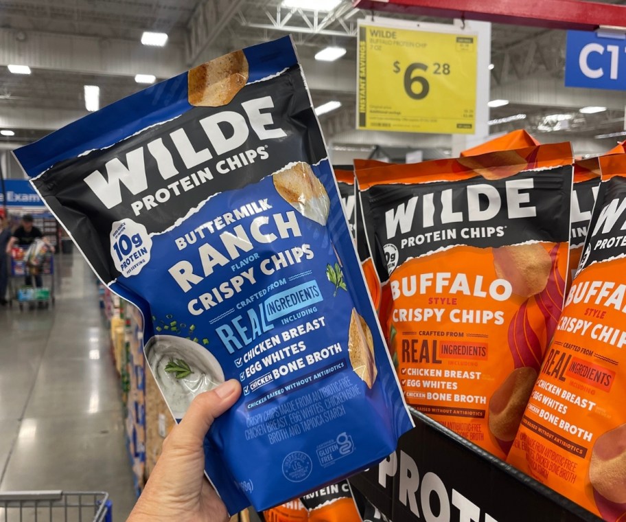 a hand holding a bag of protein chips on a store aisle